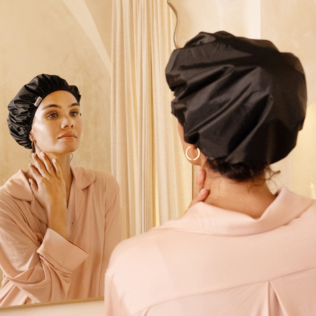 Woman wearing a black silk lined shower cap looking at herself in the mirror