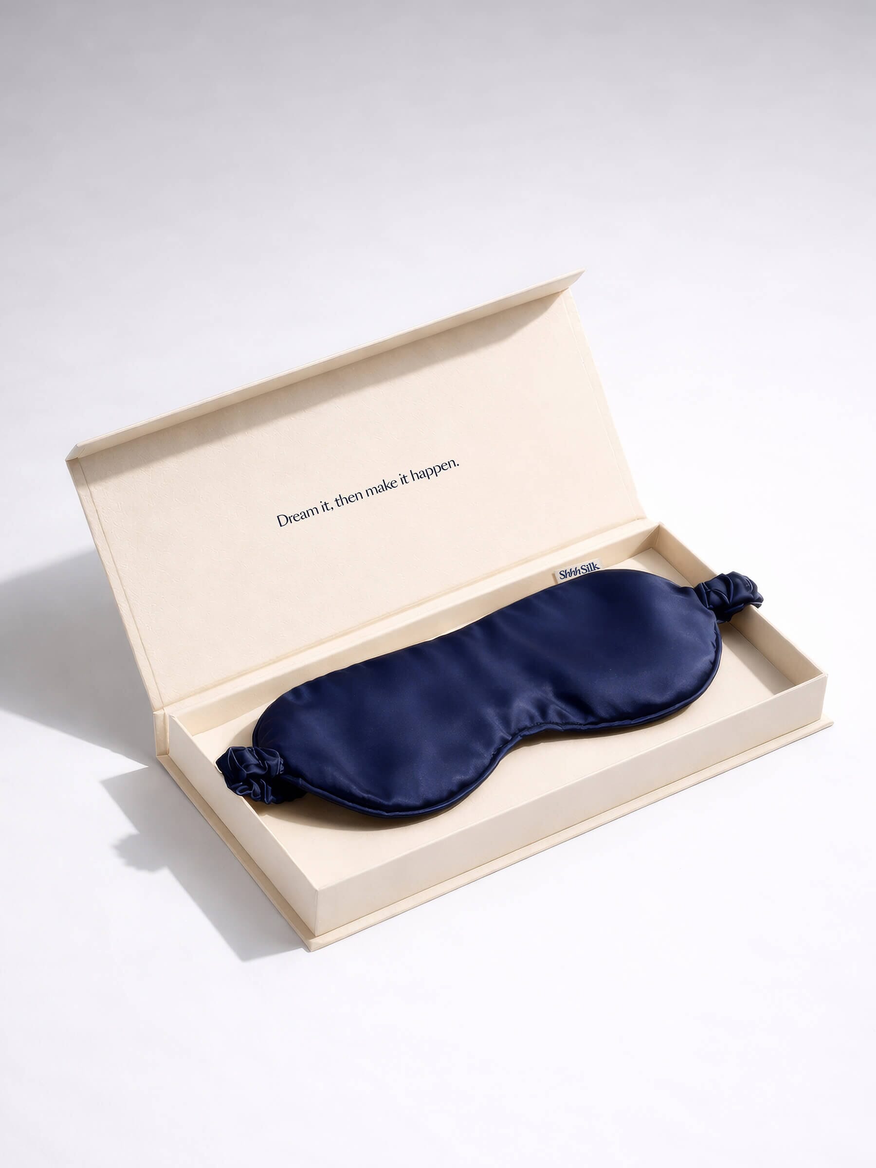 Navy silk sleep mask in an open beige box on a light grey background