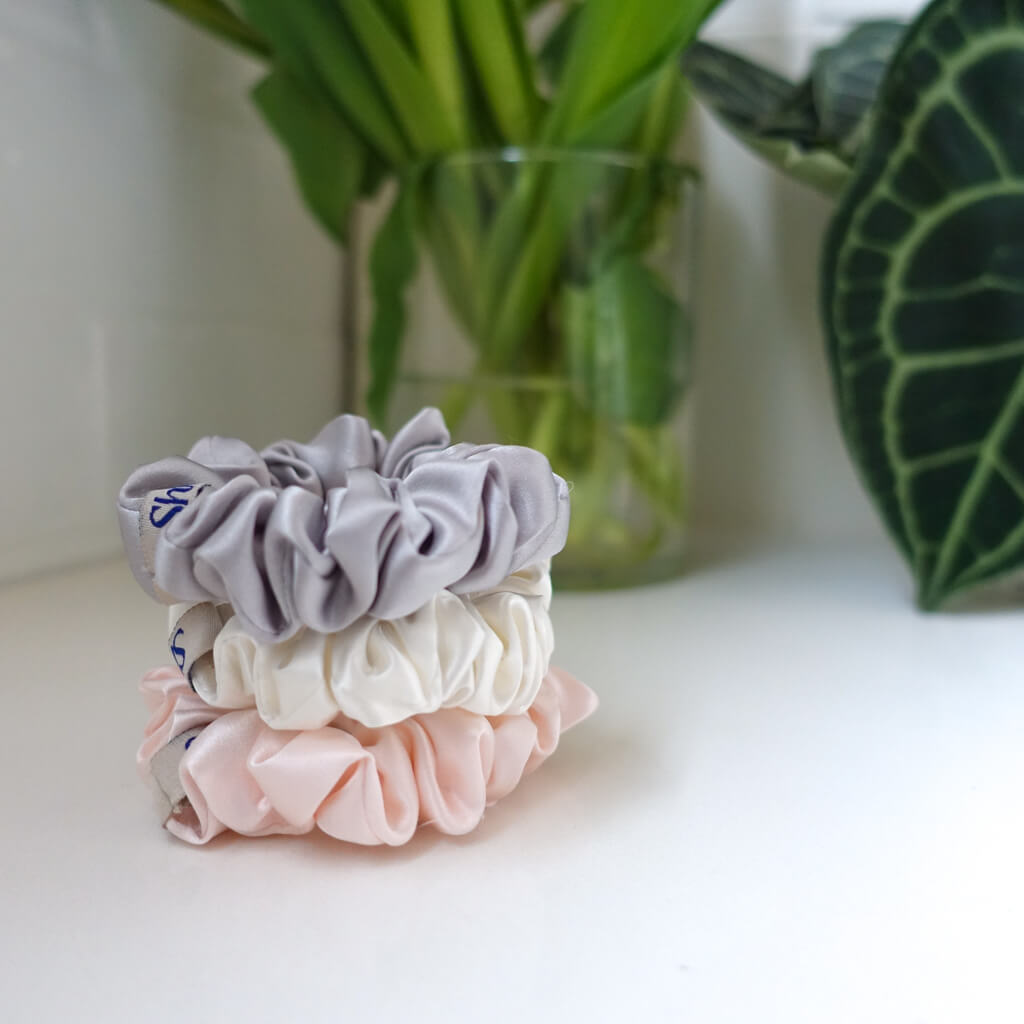 Three medium-sized silk scrunchies in grey, pink, and off-white colours