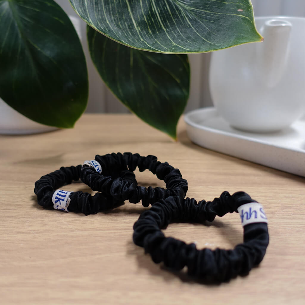 Three black mini silk scrunchies with a visible brand tag on each