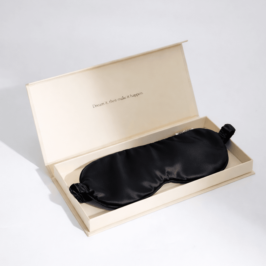 Black silk sleep mask in an open beige box on a light gray background