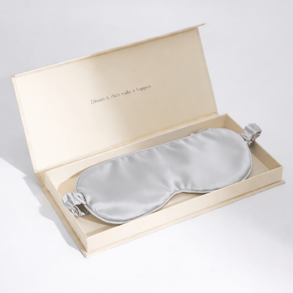Grey silk sleep mask in a beige box with text on a light grey background