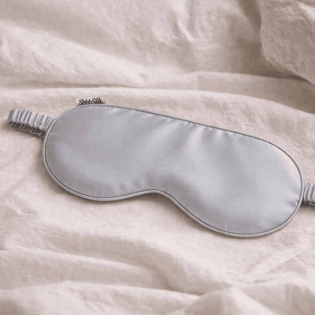 Grey silk sleep mask on a soft, light-coloured fabric background