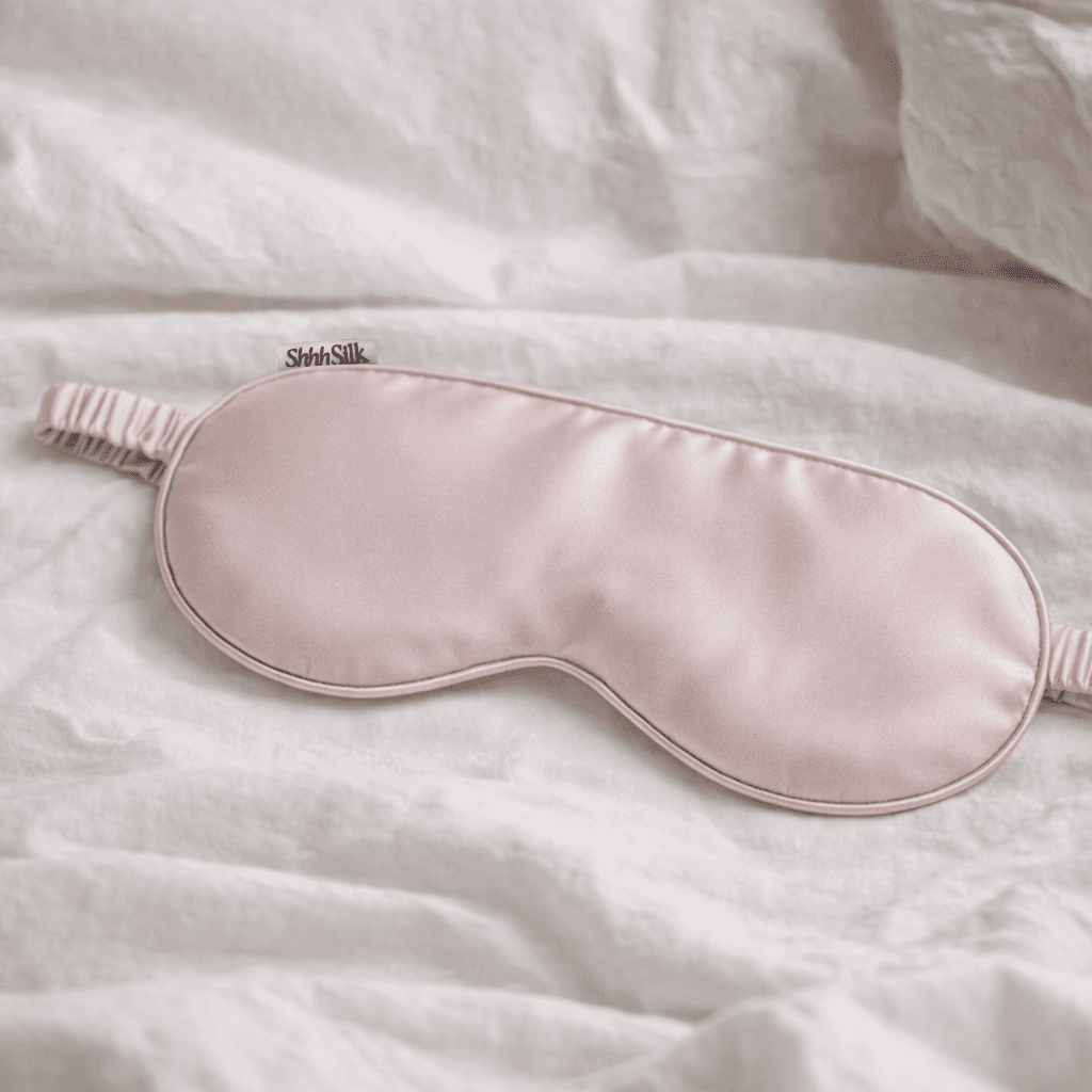 Pink silk sleep mask on a white textured surface
